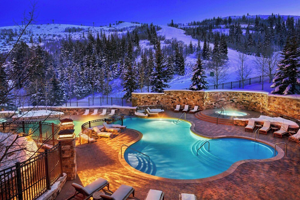 Heated outdoor pool with lounge chairs surrounded by snow-covered trees